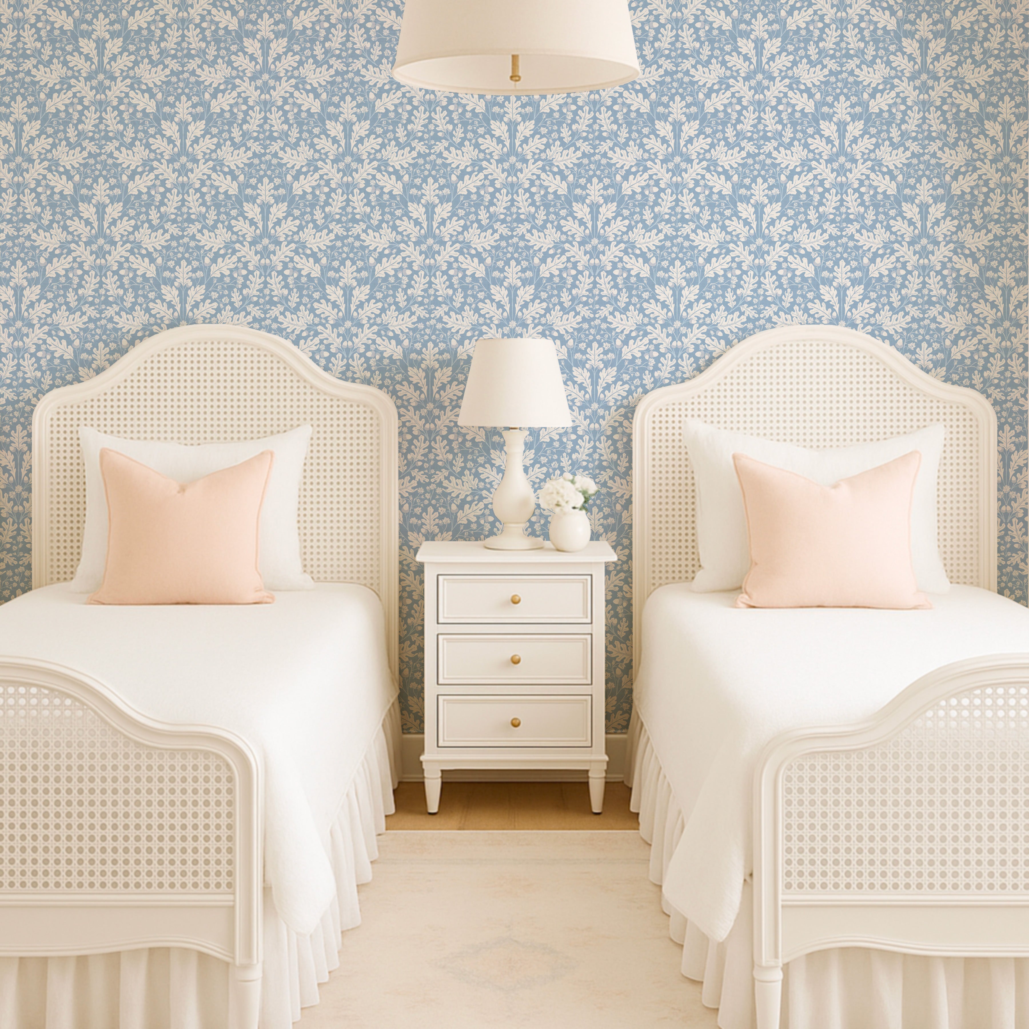 Two white beds with pink pillows in a room with floral wallpaper and a nightstand.